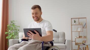 Disabled man sitting on wheelchair and talking on chat. Freelancer, young writer or student work with tablet video