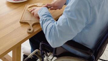 Close-up shot of a disabled person in a wheelchair cutting bread in the kitchen video