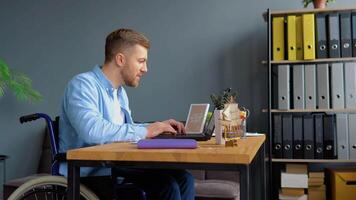 motivée désactivée la personne pigiste est travail avec portable dactylographie séance dans fauteuil roulant à bureau. loin travail et invalidité concept video