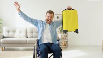 Happy disabled person in a wheelchair with a yellow suitcase in his hands is preparing for a trip. Concept of inclusion and disability video