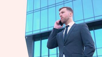 portret van gelukkig bedrijf Mens roeping telefoon buitenshuis. zakenman pratend mobiel telefoon in de buurt modern kantoor gebouw video