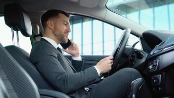 A confident man speaks on the phone sitting in a car in a business suit near a modern office building video