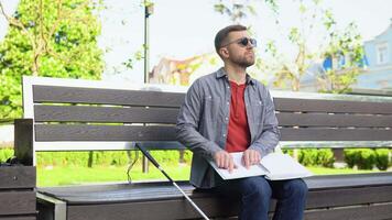 Young blind man sitting on bench in city park and reading a braille book video