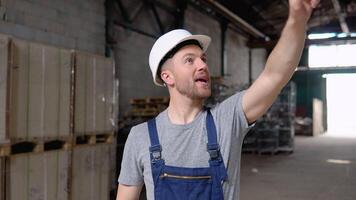 Serious manager in helmet and uniform giving commands to workers on industrial warehouse. Bearded man gesturing and shouting during working process video