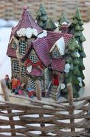 A toy diorama of small house in a winter setting surrounded by a wattle fence photo