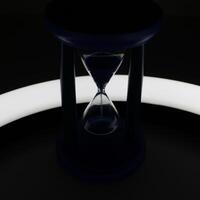 Illuminated Trickle Of Sand Inside Hourglass In Darkness Closeup View photo