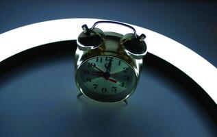 Classic copper clock with bells on a night table with LED ring lamp in darkness photo