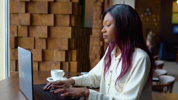 giovane africano americano donna utilizzando il computer portatile computer nel bar. femmina professionale Lavorando con taccuino video