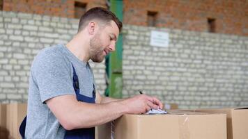 Delivery man writing something to clipboard. Courier checks the parcels on warehouse video