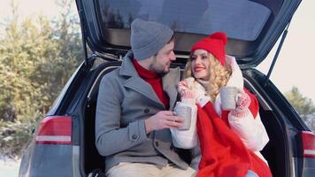 Nice couple have weekend at countryside at winter time. Sitting on the rear part of modern car. Smiling together video