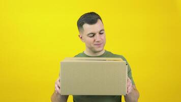 Caucasian middle-aged man in a green T-shirt lifts a craft cardboard box in front of him. The guy is standing in front of a yellow background with a parcel in his hands video