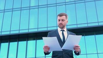 retrato do uma confiante homem dentro uma o negócio terno com documentos dentro frente do uma moderno escritório construção video