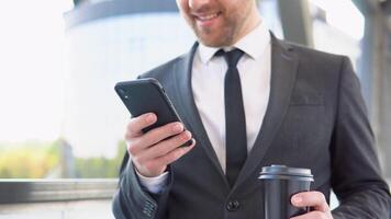 un joven confidente empresario con un café taza utilizando un móvil teléfono cerca un negocio centrar video