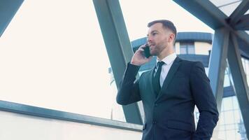 zakenman pratend mobiel telefoon in de buurt modern kantoor gebouw. portret van gelukkig bedrijf Mens roeping telefoon buitenshuis video