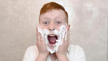 The boy smeared his cheeks with shaving foam. Funny boy in the bath smears his face with shaving cream, the child imitates an adult dad shaves video