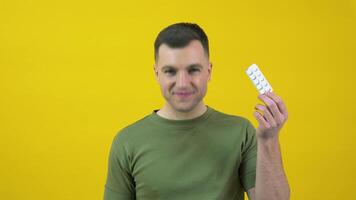 A man holding a plate of white round pills in his hand and nodding his head expresses approval, consent, support. The guy is standing in front of a yellow background with drugs in his hands video