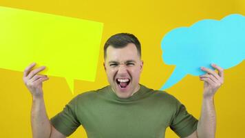 A man holds two backgrounds for the insert text and shouts loudly in the frame. The guy is standing in front of a yellow background with yellow and blue posters for text in his hands video