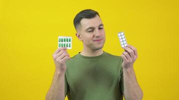 A man in holds two plates of different pills in his hands and expresses confusion. The guy is standing in front of a yellow background with drugs in his hands video