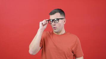 A man in glasses looks into the camera as if he can't see well. A guy in red clothes stands in front of a red background and expresses surprise video