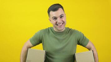 Caucasian middle-aged man in a green T-shirt holding two craft cardboard boxes. The guy is standing in front of a yellow background with 2 parcels in his hands. Yellow-green color scheme video