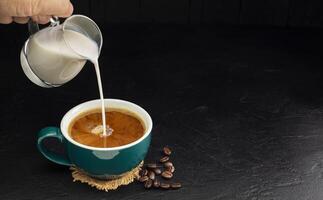 Leche crema vertido dentro un verde café taza en un de madera mesa, negro y oscuro antecedentes. foto