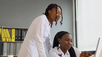 zwei afrikanisch Frauen Studenten diskutieren geduldig Behandlung planen zeigen etwas auf Laptop. online Behandlung video