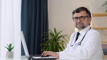 Senior doctor 50s works in laptop. Old mature doctor therapist working at office video