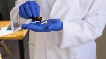 Senior female doctor in white coat takes pills out of a jar. Close up view of hands video