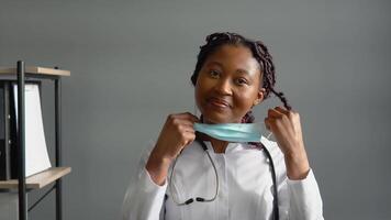 Positive african female doctor removes a medical mask in clinic. End of quarantine. Stop virus video