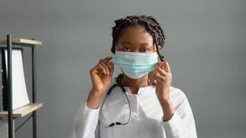 joven africano americano hembra médico pone en un protector azul mascarilla. virus proteccion video