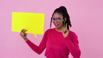 Cute young african american girl stands with posters for expression on a solid pink background. A place for advertising slogans video