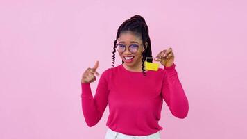 joven africano americano niña en rosado ropa participación un mini juguete compras cesta. adolescente niña ama de casa principiante en pie en un sólido rosado antecedentes video