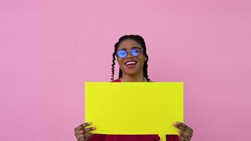 Young african american girl stands with posters for expression on a solid pink background. A place for advertising slogans video