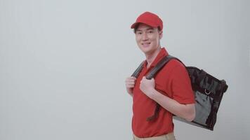 asiático joven comida entrega hombre vistiendo rojo uniforme que lleva comida equipaje sonriente en blanco antecedentes video