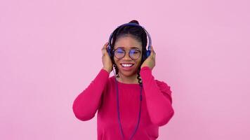 linda joven africano americano música amante niña es escuchando a música desde teléfono inteligente en foto estudio. adolescente niña en rosado ropa bailes en un sólido rosado antecedentes video