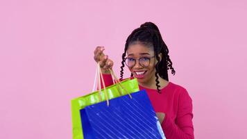 jovem africano americano menina dentro Rosa roupas tendo Diversão e dançando com papel laminado bolsas com alças. adolescente menina em pé em uma sólido Rosa fundo video