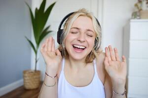 Close up portrait of candid, happy young woman in headphones, singing and listening to music at home photo