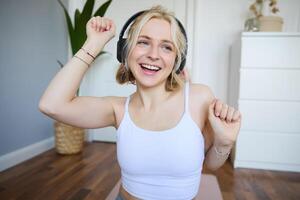 Portrait of charismatic, beautiful young woman dancing and listening to music in wireless headphones, singing along favourite song in her room photo
