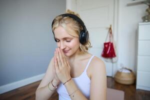 retrato de joven relajado mujer, se sienta en habitación en auriculares, corchete manos juntos, meditado, escucha a yoga música foto