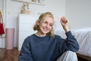 Portrait of beautiful and stylish young woman, vlogger recording on her digital camera in a room, showing beauty products, making makeup tutorial for followers on social media photo