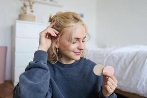 Portrait of young woman chatting on live stream about makeup, sits on floor in bedroom, showing beauty products to followers photo