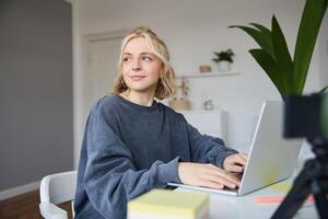 Portrait of smiling young woman, college student sits in her room, does homework, studies remotely from home, uses laptop for freelance work photo