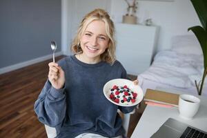 Portrait of young woman talking to audience, recording vlog on digital camera, showing her breakfast, talking about healthy food and lifestyle photo