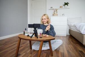 Portrait of beautiful smiling woman, recording in her room, has camera on coffee table, reviewing makeup, doing lifestyle vlog for social media account, records a tutorial photo