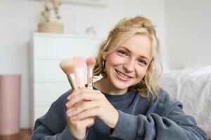 Close up portrait of cute teen girl showing her beauty makeup brushes, smiling and looking at camera photo