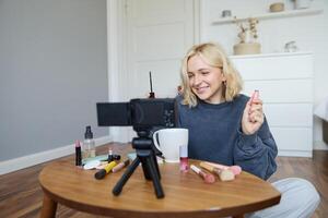 retrato de rubio sonriente mujer registros un estilo de vida Blog, vlogger o maquillaje artista grabación para social medios de comunicación, participación máscara, revisando belleza productos para seguidores en línea foto