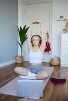 Portrait of young fitness woman doing warm-up exercises, looking at workout on laptop, stretching arms, wearing headphones photo