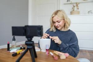 retrato de joven sonriente mujer en su habitación, grabación en cámara, estilo de vida vlog para social medios de comunicación, participación máscara, revisando su maquillaje belleza productos, demostración cómo a utilizar productos cosméticos foto