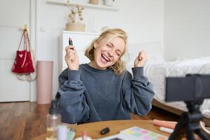 Portrait of young content creator, woman with social media account, recording about makeup on digital camera, holding favorite lipstick, recommending product to audience online photo