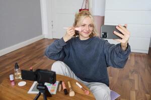 Portrait of beautiful blond girl doing makeup on camera, recording vlog using digital camera and live stream on mobile phone app, chatting with audience photo